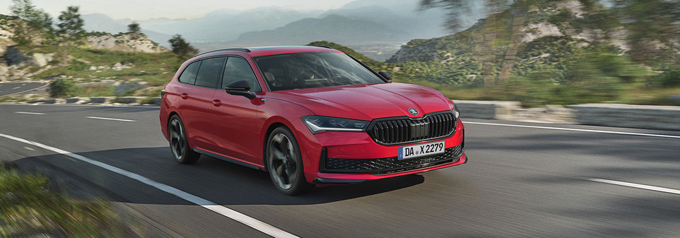 Ein Škoda Superb Combi Sportline in Rot fährt außerorts, mit Gebirgen im Hintergrund.